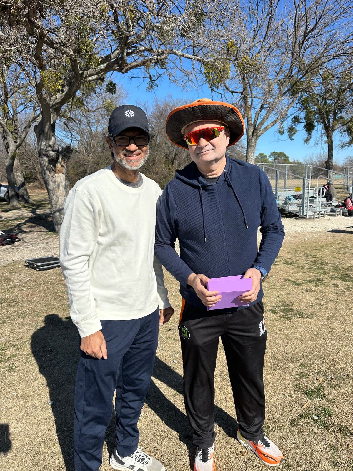 Two men standing beside the ground on a bright winter day, one holding a box of bail guard packets.