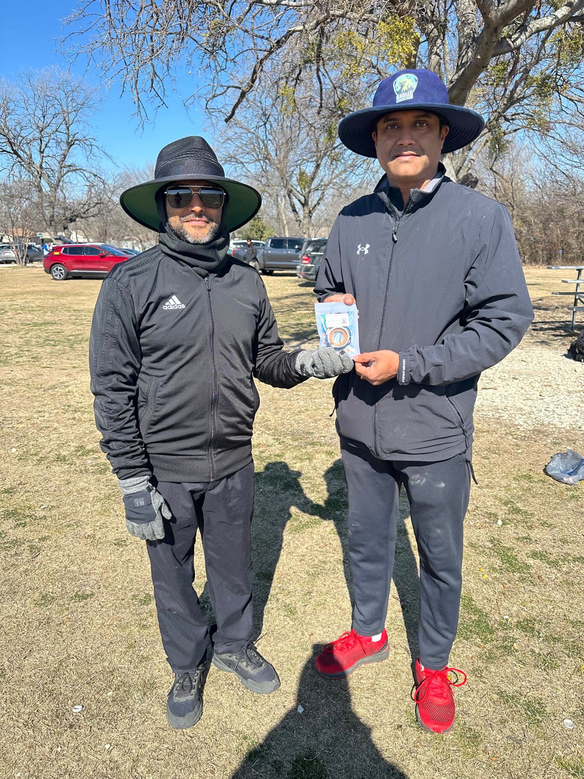 Two umpires in cold weather gear and wide brimmed hats, holding a bail guard packet between them.