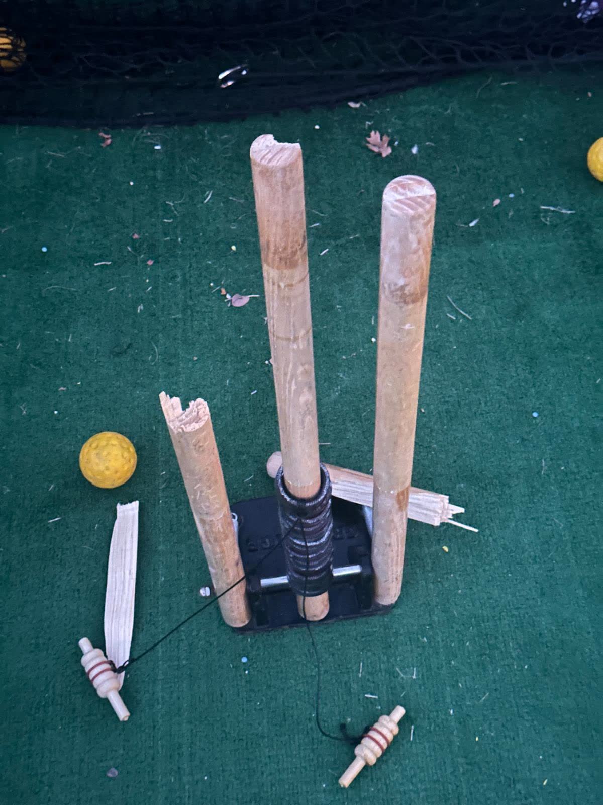 After an impact test: the off stump snapped in two on the matting, the middle stump still standing with the bail guard collar wrapped around it, tethered bails lying either side.